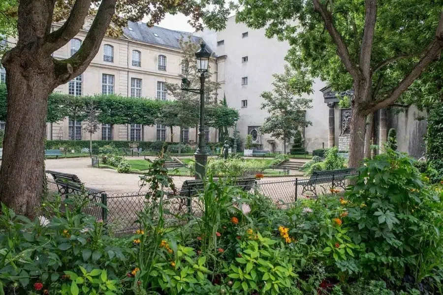 “Hidden rose garden at Square Georges Cain in the Marais, Paris, a quiet green space with historic statues.”